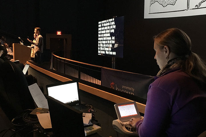 Stenographer listening to speaker, captions displayed on screen